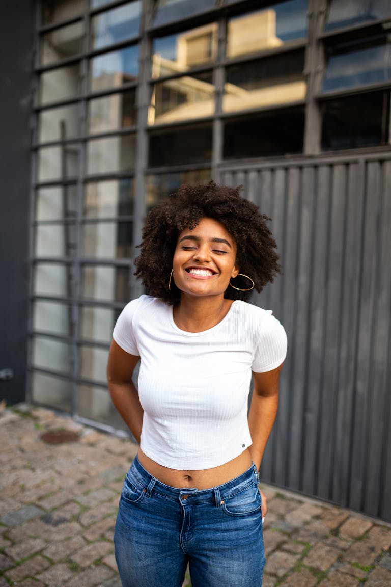 Smiling woman with curly hair in casual fashion enjoys a bright day outdoors.